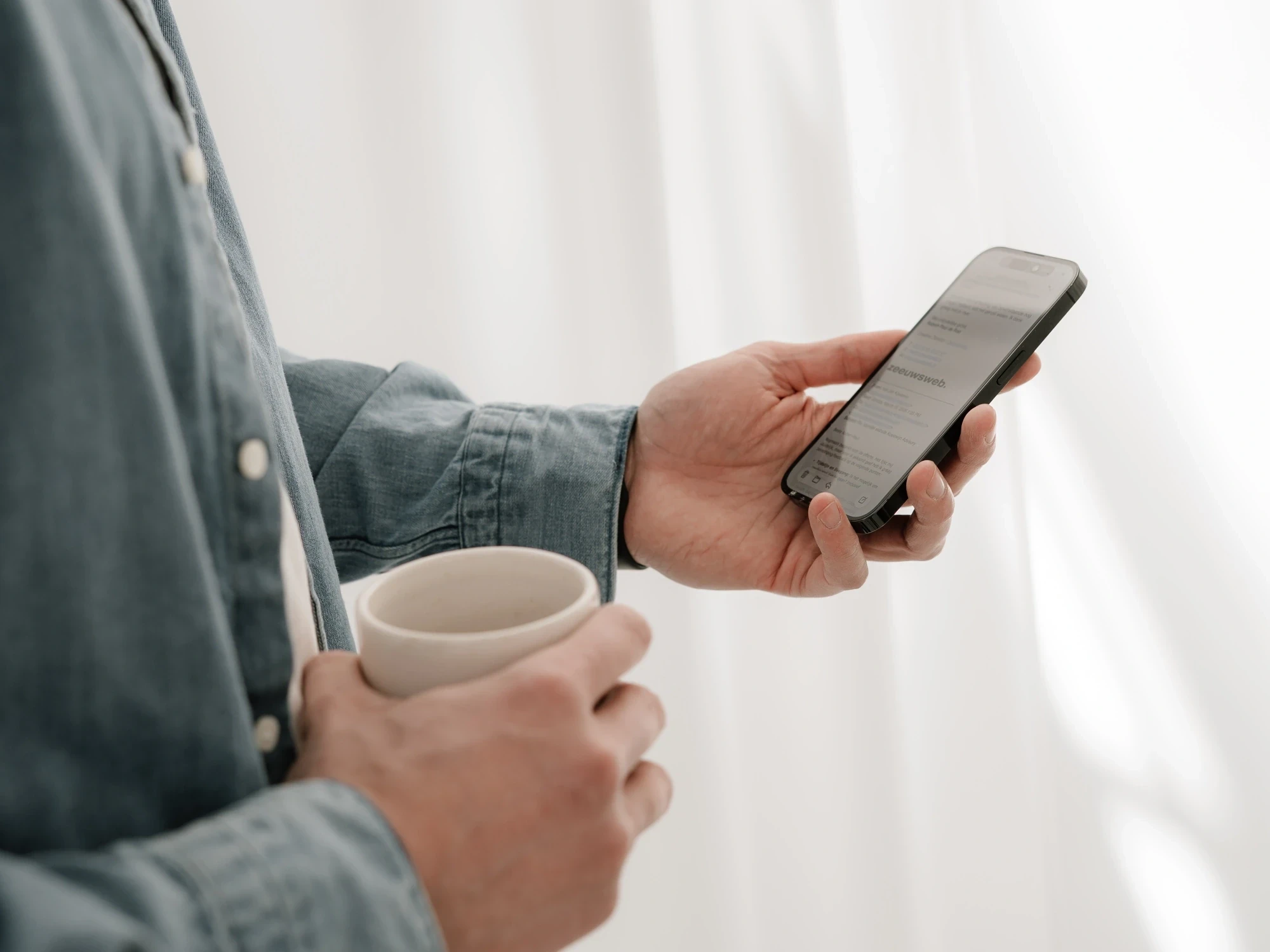 Een e-mail van Zeeuwsweb op een telefoon, met een kop koffie in de andere hand