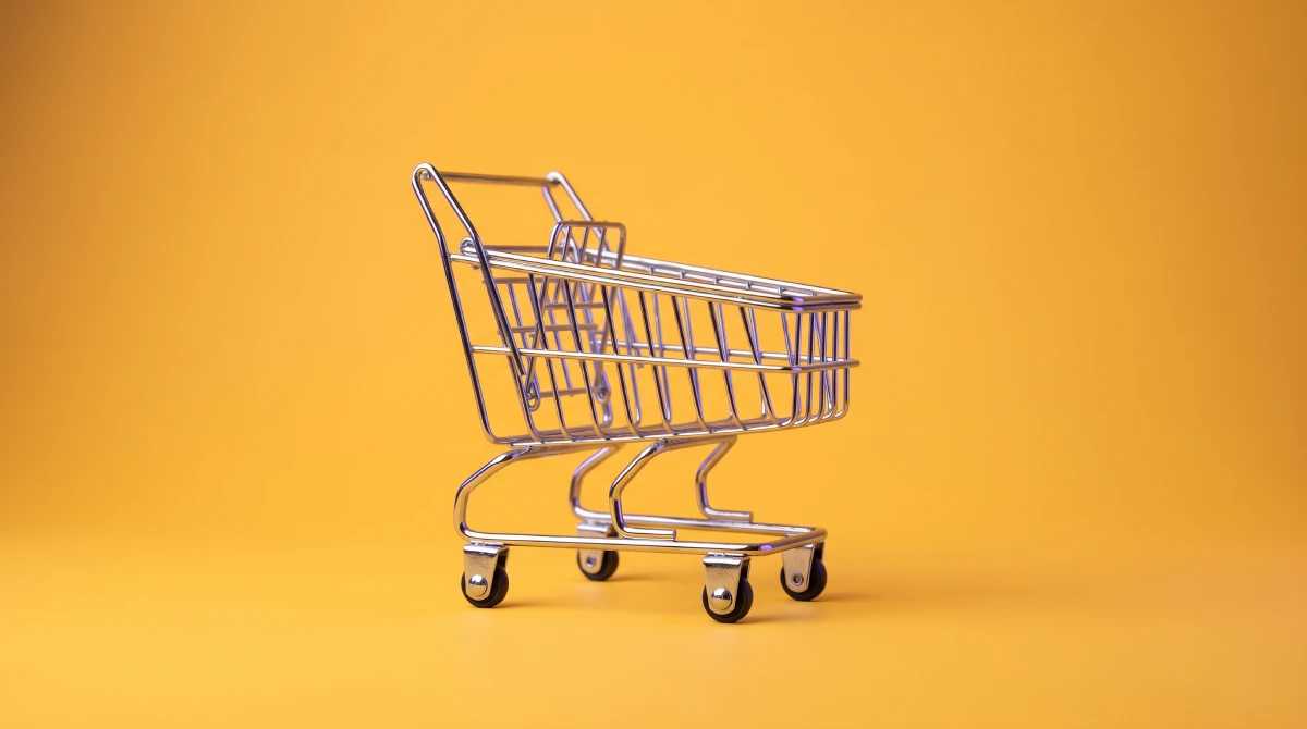 Een klein metalen winkelwagentje op een gele achtergrond, als beeld bij een webwinkel laten maken